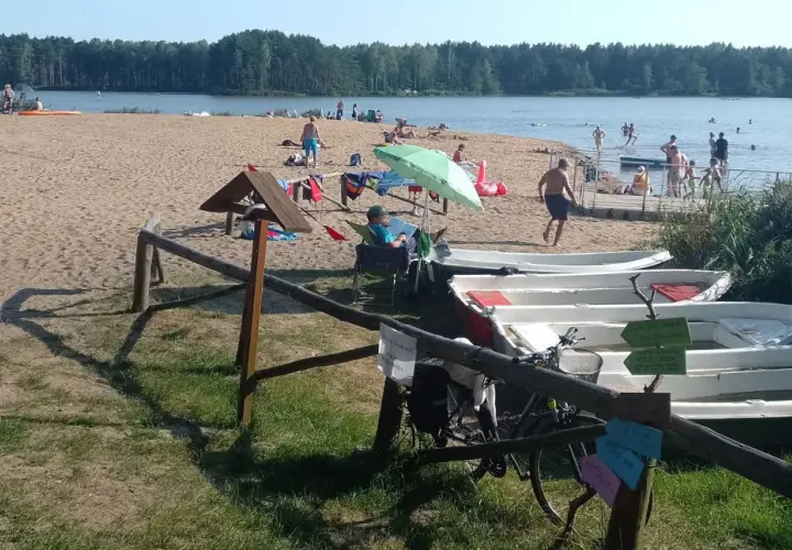 Słoneczny dzień nad zalewem zielona. Ludzie odpoczywają na plaży, kąpią się, a obok stoją łódki.