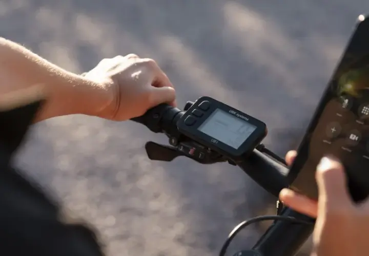 Rowerzysta trzyma kierownicę, na której zamontowany jest licznik rowerowy nie pokazuje prędkości. Obok wyświetlacz telefonu z połączeniem do Valerie.