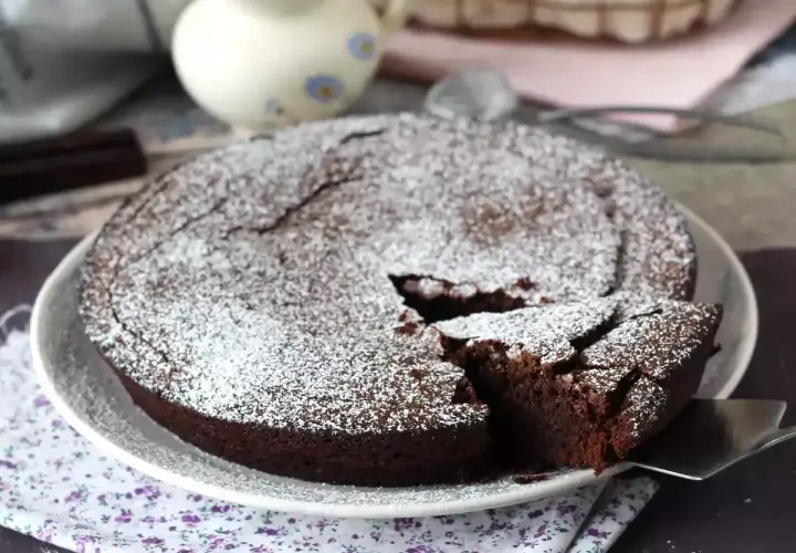 Un délicieux gâteau au chocolat saupoudré de sucre glace, parfait pour une recette gâteau au chocolat facile. Une part est coupée.