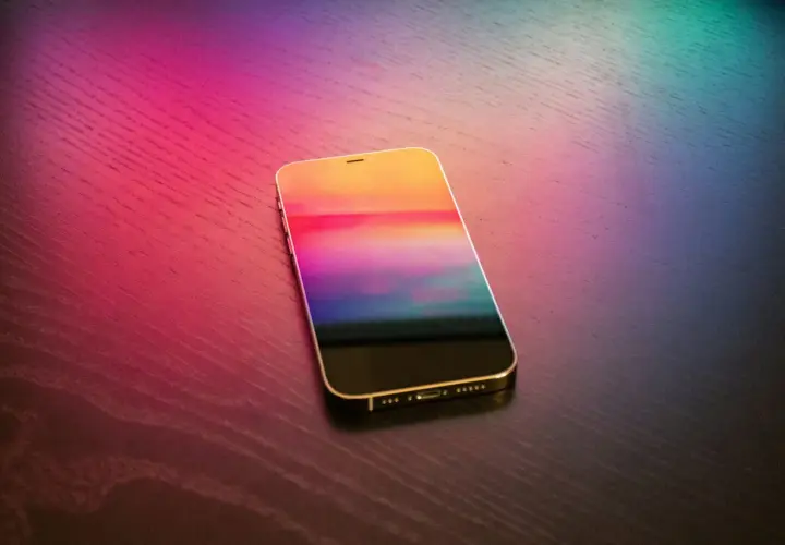 Złoty iPhone z kolorowym ekranem na drewnianym blacie. Dowiedz się, jak wgrać dzwonek na iPhone bez iTunes.
