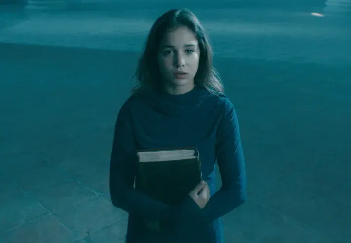 Alba Baptista, med en gammal bok i famnen, ser fundersam ut i det blåa ljuset.