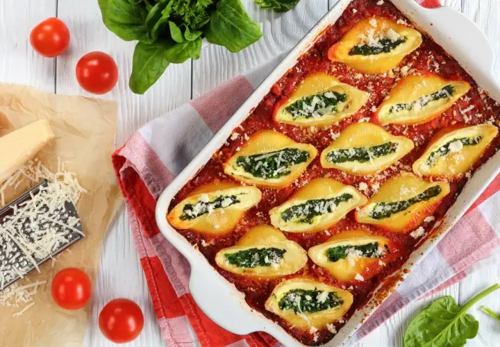 Makaron conchiglioni faszerowany szpinakiem i serem w sosie pomidorowym, podany w naczyniu żaroodpornym.