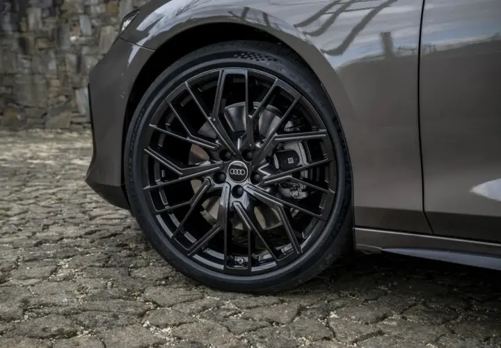 Zbliżenie na czarne felgi Audi z oponami na kamiennej nawierzchni.