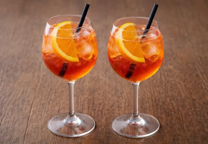 Dwa Aperol Spritz z pomarańczą i lodem, idealne aperol proporcje na drewnianym tle.