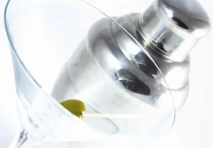 Verre à martini avec une olive, prêt pour une recette de martini gin. Shaker à cocktail en arrière-plan.