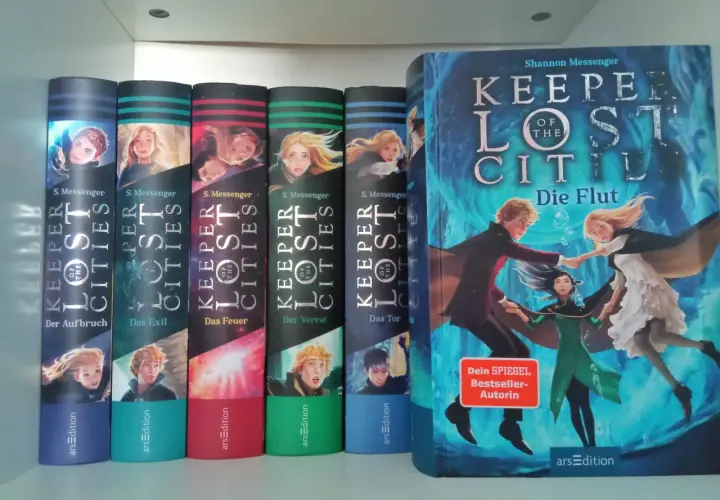 Die Bücherreihe "Keeper of the Lost Cities" mit Sophie als Hauptfigur. Mehrere Bände sind nebeneinander aufgestellt, der größte Band "Die Flut" steht rechts.