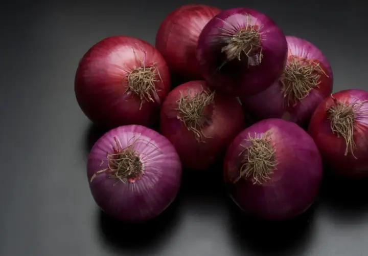 Un grupo de cebollas rojas sobre fondo oscuro. Se rumorea que el champú de cebolla tiene propiedades beneficiosas para el cabello.