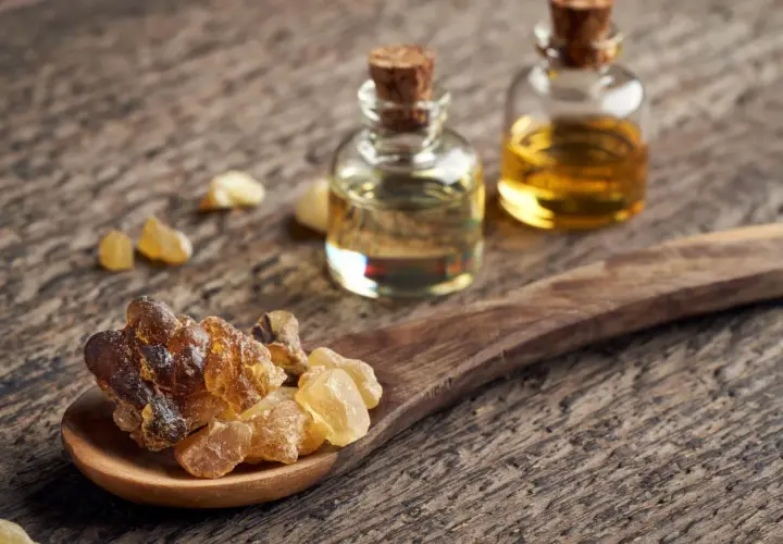 Resina di Boswellia Serrata su cucchiaio di legno, accanto a boccette di olio essenziale. Un integratore naturale.