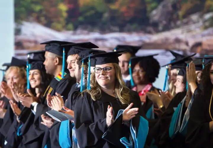 Graduates in caps and gowns applaud, celebrating their achievements in the UNC Chapel Hill online MPA program.