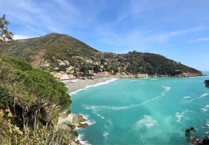 Vue panoramique de la baie de Bonassola en Italie, avec ses eaux turquoise, sa plage animée et ses collines verdoyantes couvertes de maisons.