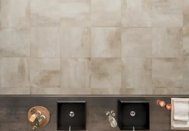 Bagno moderno con due lavabi neri, accessori e un rivestimento in gres tutta massa effetto pietra.