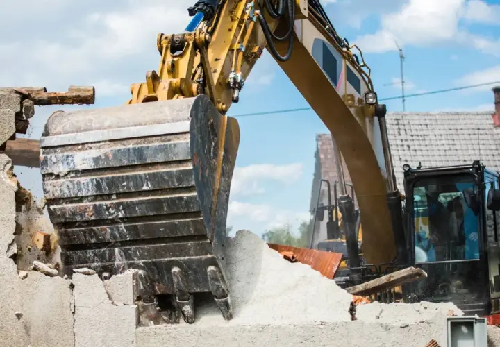 Une pelleteuse jaune démolit une maison. Le prix de la démolition maison est en cours de calcul.