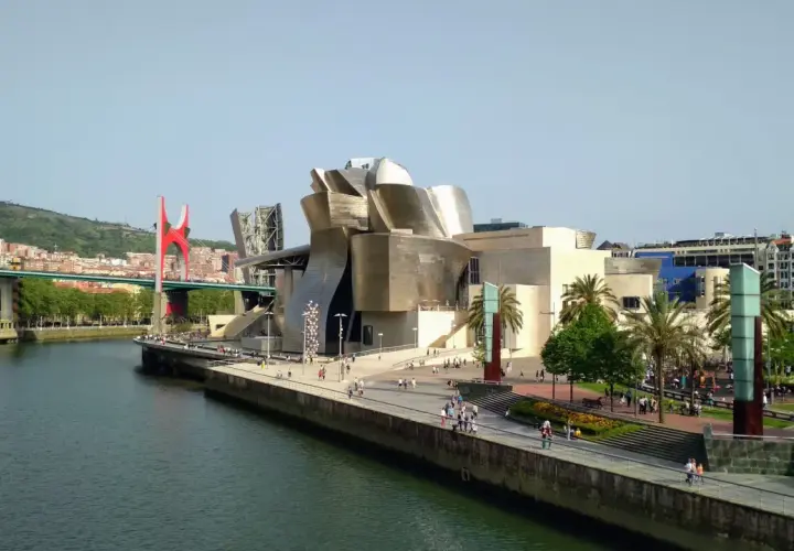 Museo Guggenheim y puente rojo, ideal para saber qué ver en Bilbao en 1 día. Paseo junto a la ría con gente disfrutando del sol.
