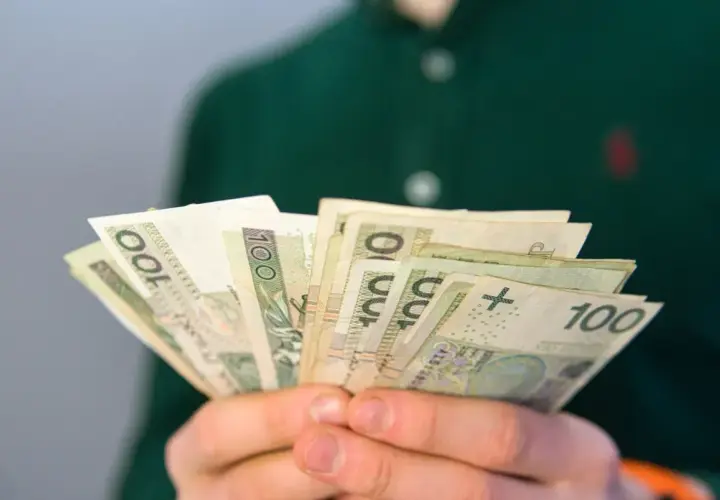 Dłonie trzymają wachlarz banknotów 100 zł. To może być pomocne przy pytaniu, co to jest renta rodzinna.