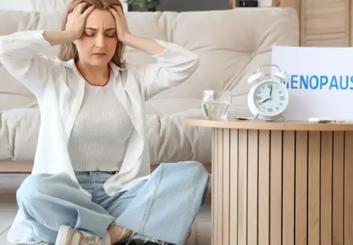 Kobieta z bólem głowy podczas menopauzy, obok tabletki i budzik.