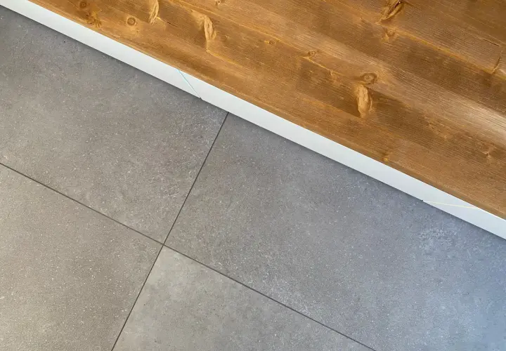 Le piastrelle grigie con venature sottili si incontrano sotto un piano in legno scuro, creando un contrasto moderno.