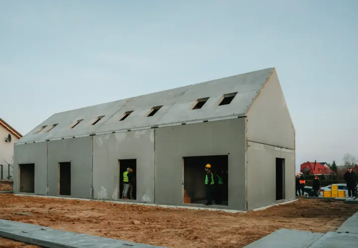 Budowa domu z gotowych elementów betonowych. Widać pracowników w kamizelkach odblaskowych.