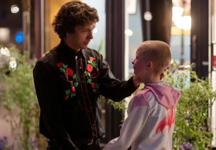 En man med blommig skjorta rör vid ett barns kind. En scen som kan ingå i svenska komedier.