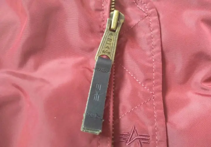 Zamek kurtki Alpha Industries z logo. Detale materiału i szwów, pomocne przy wyborze alpha industries rozmiarówka.