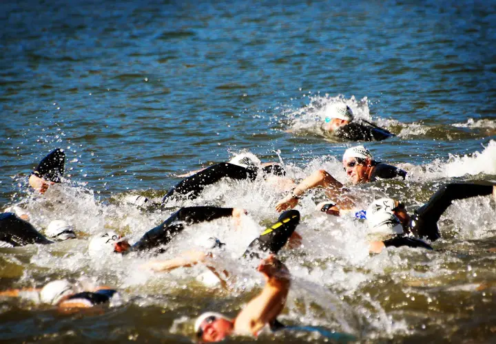 Zawodnicy walczą o pozycję podczas pływania na dystansie 1/2 ironman. Woda wzburzona, widać kaski i okulary.