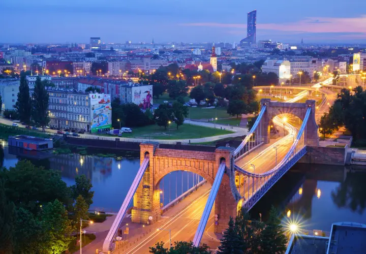 Most Wrocławia w niebieskiej godzinie w fotografii. Most Grunwaldzki i miejska panorama nocą, z rozmazanymi światłami samochodów tworzącymi smugi.