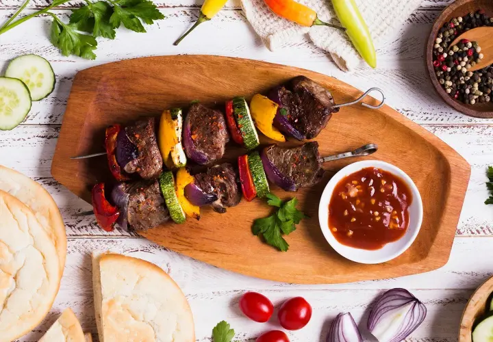 Brochette de rumsteck grillée avec poivrons, courgettes et oignons, servie avec une sauce savoureuse.