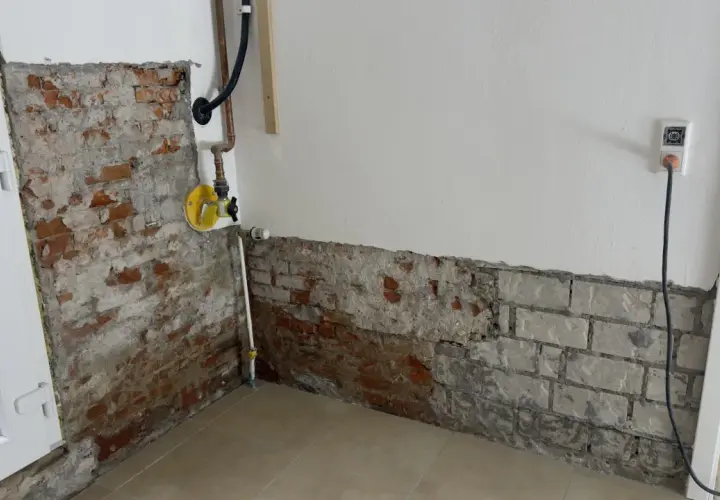 Baustelle mit freiliegendem Mauerwerk und Rohren. Ein gelbes Ventil deutet auf eine bevorstehende Maßnahme wie das Injektionsverfahren Horizontalsperre hin.