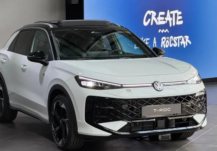 Biały Volkswagen T-Roc z czarnym dachem i felgami. Na ekranie w tle napis "CREATE LIKE A ROCSTAR". Sprawdź aktualną volkswagen t-roc cena.