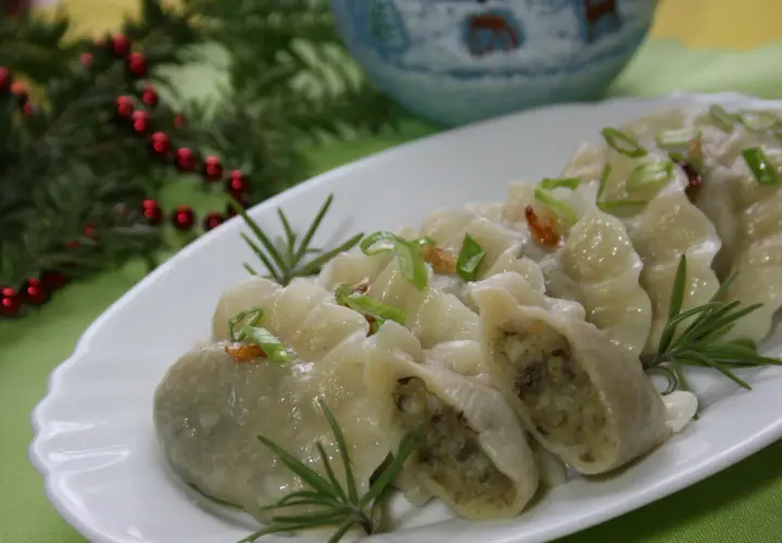 Pyszne, domowe pierogi ukraińskie, udekorowane szczypiorkiem i rozmarynem, prezentują się apetycznie na białym talerzu.