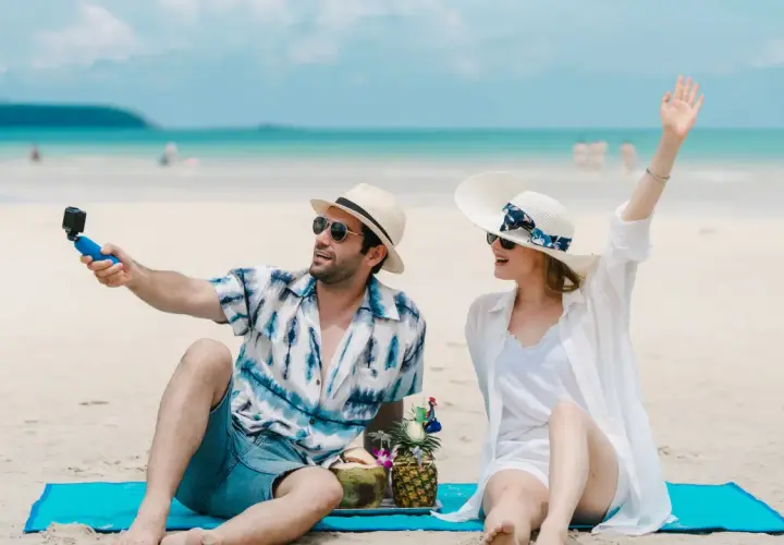Para w letnich strojach robi sobie selfie na plaży, z napojami i owocami. To idealne wczasy pod gruszą!