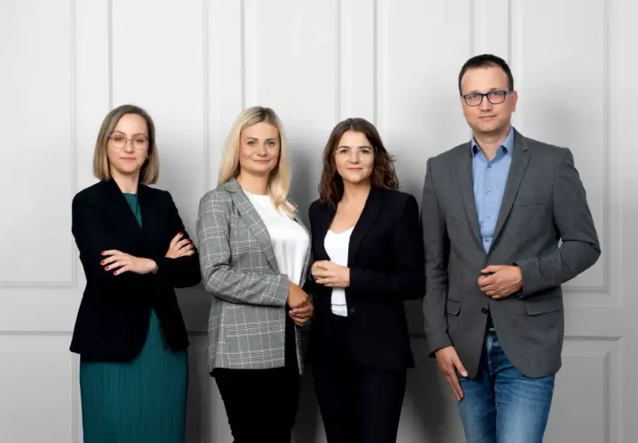 Cztery osoby w strojach biznesowych stoją obok siebie na jasnym tle.