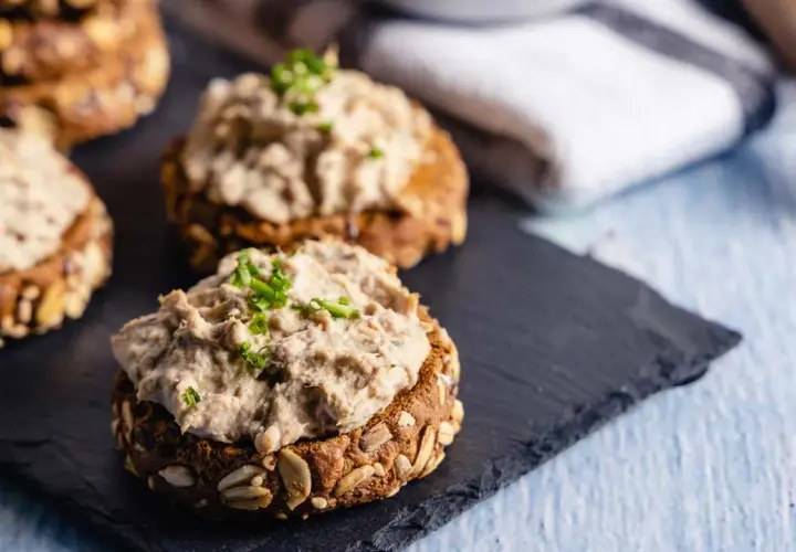 Deliciosos canapés con atún vegano cremoso y cebollino fresco sobre pan integral con semillas.