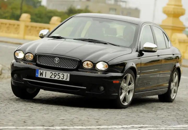 Czarny Jaguar X Type na brukowanej ulicy, z charakterystyczną atrapą chłodnicy i okrągłymi reflektorami.