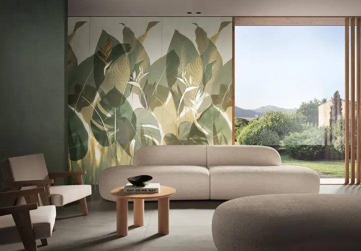 Soggiorno con divano beige e poltrone in legno, parete con fap rivestimenti a tema foglie tropicali e vista su giardino lussureggiante.