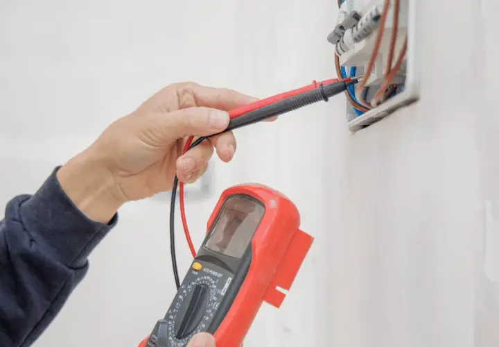 Elektryk sprawdza instalację elektryczną multimetrem, przygotowując protokół odbioru.