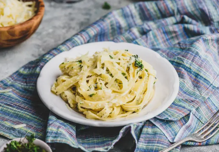 Pyszny makaron z pancettą, kremowym sosem i startym parmezanem, podany na talerzu z kolorową serwetką.