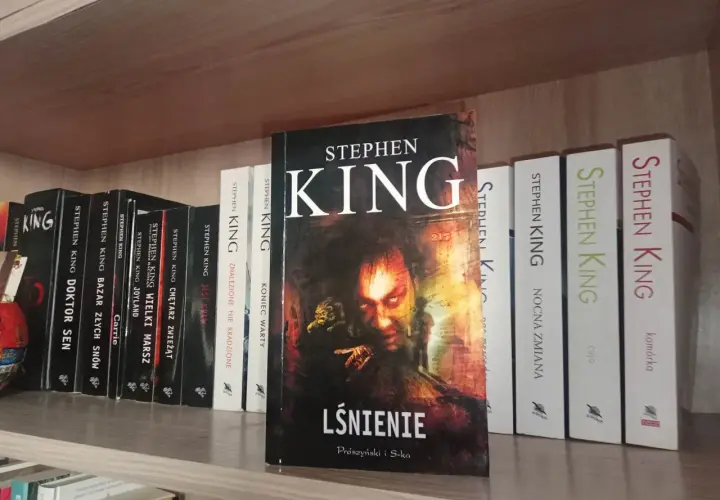 Książki Stephena Kinga na półce, w tym "Lśnienie" z przerażającą okładką.