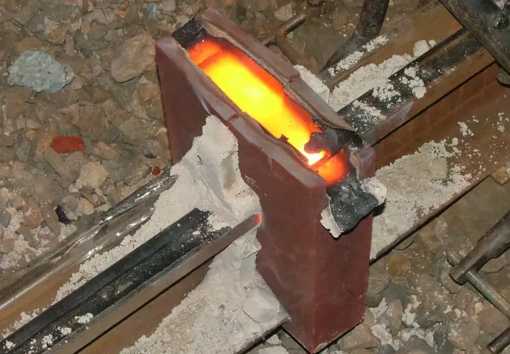 Żelazny szynoprzewód połączony metodą spawania termitowego. Roztopiony metal płynie w formie, tworząc mocne połączenie.