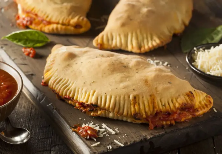 Pyszny calzone z kurczakiem, sos pomidorowy, starty ser i świeża bazylia na drewnianej desce.