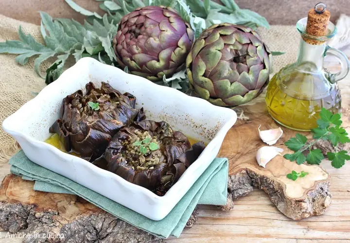 Carciofi al forno morbidi ripieni, serviti in una teglia bianca con olio d'oliva, aglio e prezzemolo.