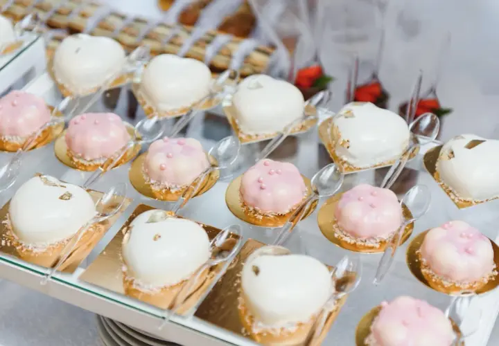 Eleganckie finger food w kieliszkach: serduszka i kwiatki w białej i różowej polewie, ozdobione perełkami i płatkami złota.