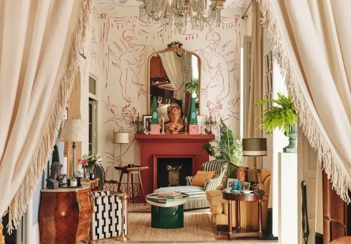 Salon éclectique avec papier peint aux figures rouges, cheminée rouge, mobilier ancien et moderne, rideaux à franges.