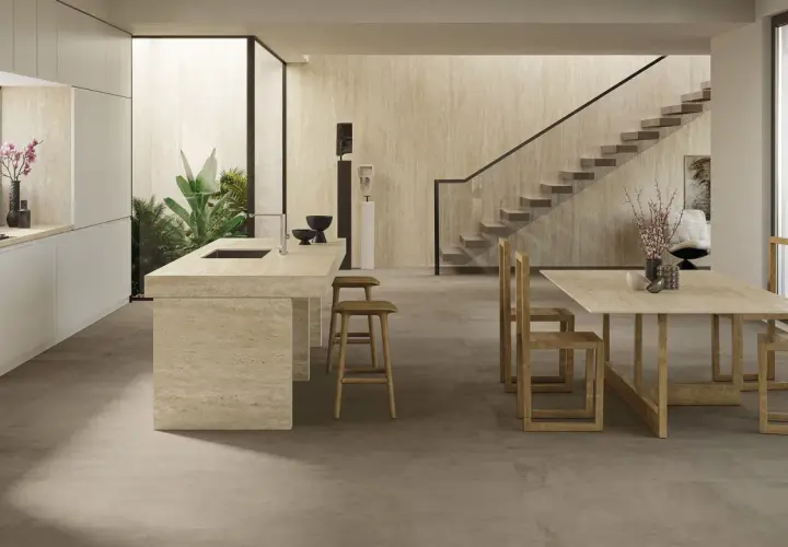 Cucina moderna con isola in travertino e tavolo in legno. Il pavimento non rettificato crea un effetto materico e continuo, integrandosi con le pareti in pietra.