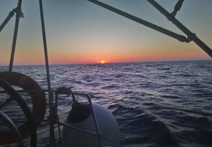 Zachód słońca nad wzburzonym oceanem atlantyckim widziany z pokładu żaglówki. Widać koło ratunkowe i ster.
