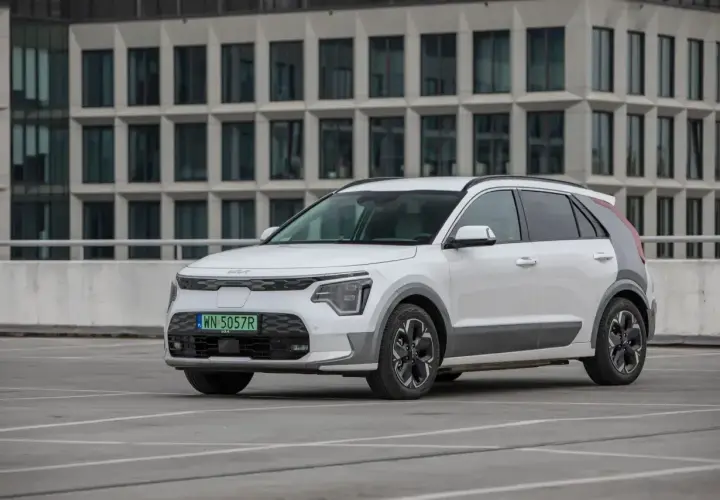Białe Kia Niro stoi na parkingu przed nowoczesnym budynkiem. Sprawdź kia niro wymiary, by poznać jego gabaryty.