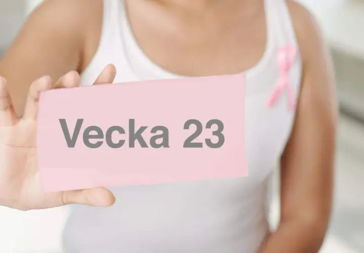 En person håller upp en rosa lapp med texten "Vecka 23". En rosa band pryder personens vita linne.