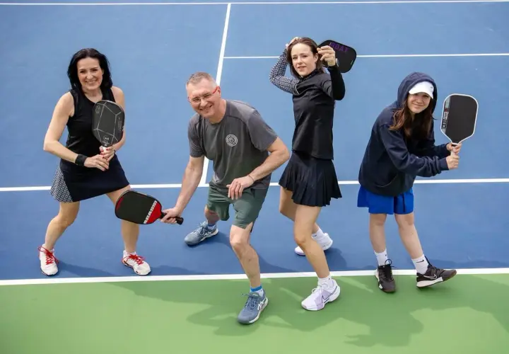 Rodzina na korcie do pickleball, co to za sport? Wszyscy trzymają rakietki, gotowi do gry.