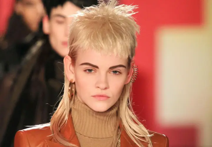 Model mit modernem Mullet-Haarschnitt, braunem Rollkragenpullover und Lederjacke. Goldene Ohrringe und auffälliger Ohrschmuck.
