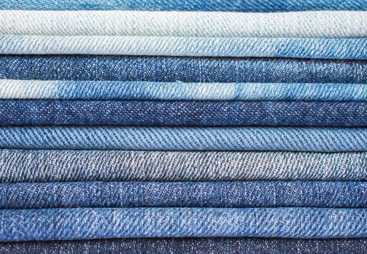 Pile de jeans bleus de différentes teintes. Le jean est fait de coton, un tissu résistant et confortable.