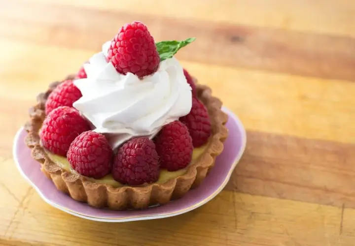Tartelette garnie de framboises fraîches et d'une délicate crème chantilly, évoquant l'origine d'une douceur intemporelle.